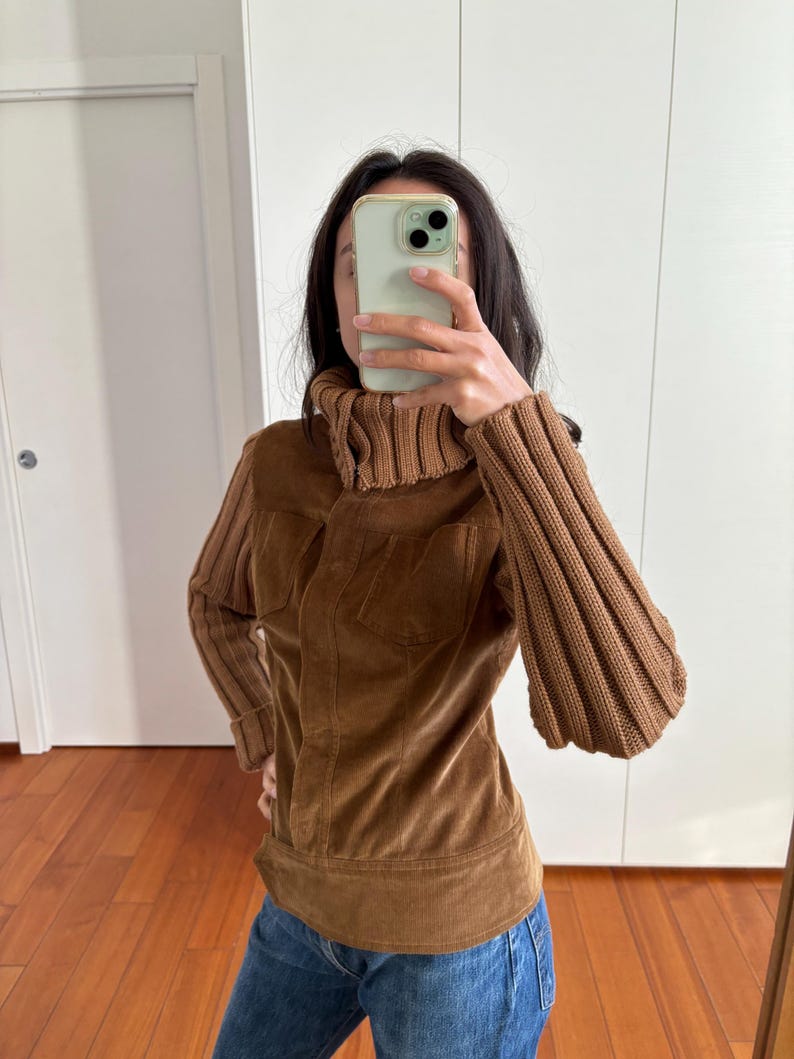 May include: A brown corduroy jacket with a turtleneck collar and ribbed knit sleeves. The jacket has a zipper closure and a fitted silhouette.