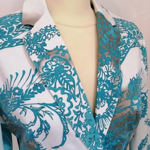 May include: A white blazer with a teal and silver floral pattern. The blazer has a single button closure and a notched collar.