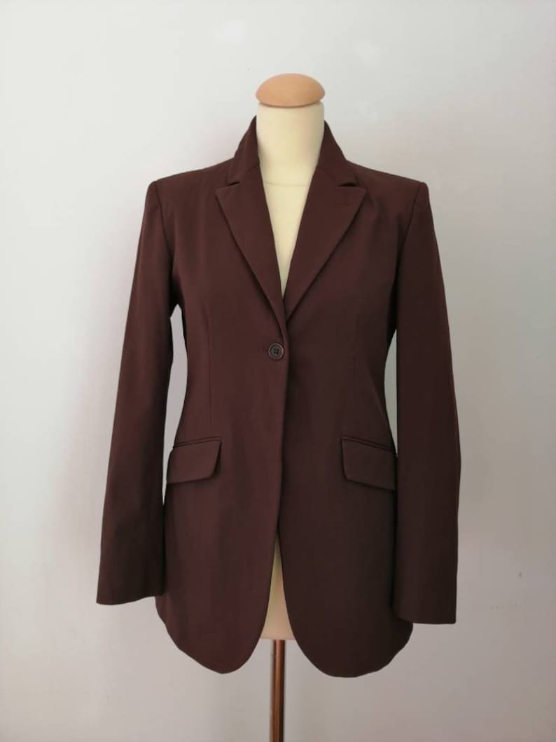 Pu&ograve; includere: Un blazer marrone con una chiusura a bottone singolo e due tasche. Il blazer ha una vestibilit&agrave; classica e sartoriale.