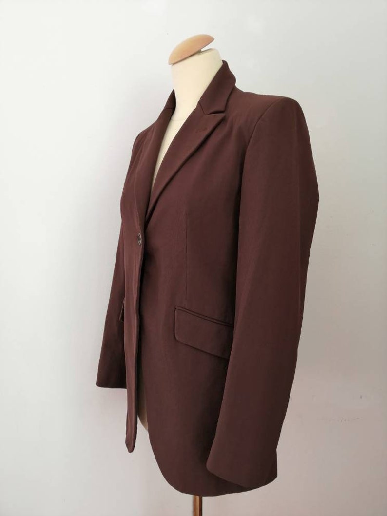 Pu&ograve; includere: Un blazer marrone con un solo bottone di chiusura e un colletto a punta.