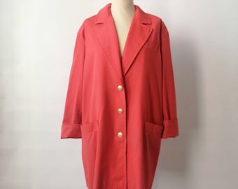 May include: A coral-colored blazer with gold buttons and two front pockets. The long-sleeved jacket is displayed on a wooden mannequin. The sleeves are cuffed at the wrists. The blazer has a classic lapel collar.