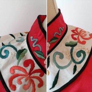 May include: Close-up of a red and white embroidered collar with a black trim. The collar features a floral design with green leaves and a blue swirl.