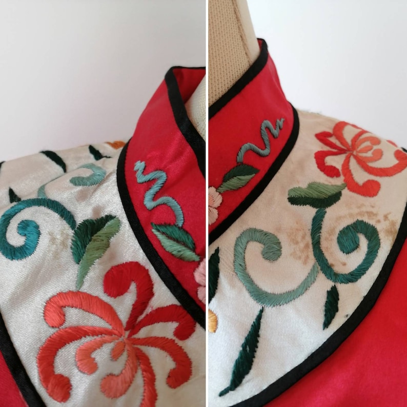 May include: Close-up of a red and white embroidered collar with a black trim. The collar features a floral design with green leaves and a blue swirl.