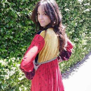 Puede incluir: Una mujer con un vestido de retazos rojo, amarillo, azul y marr&oacute;n con estampado floral. El vestido tiene manga larga y falda fruncida.
