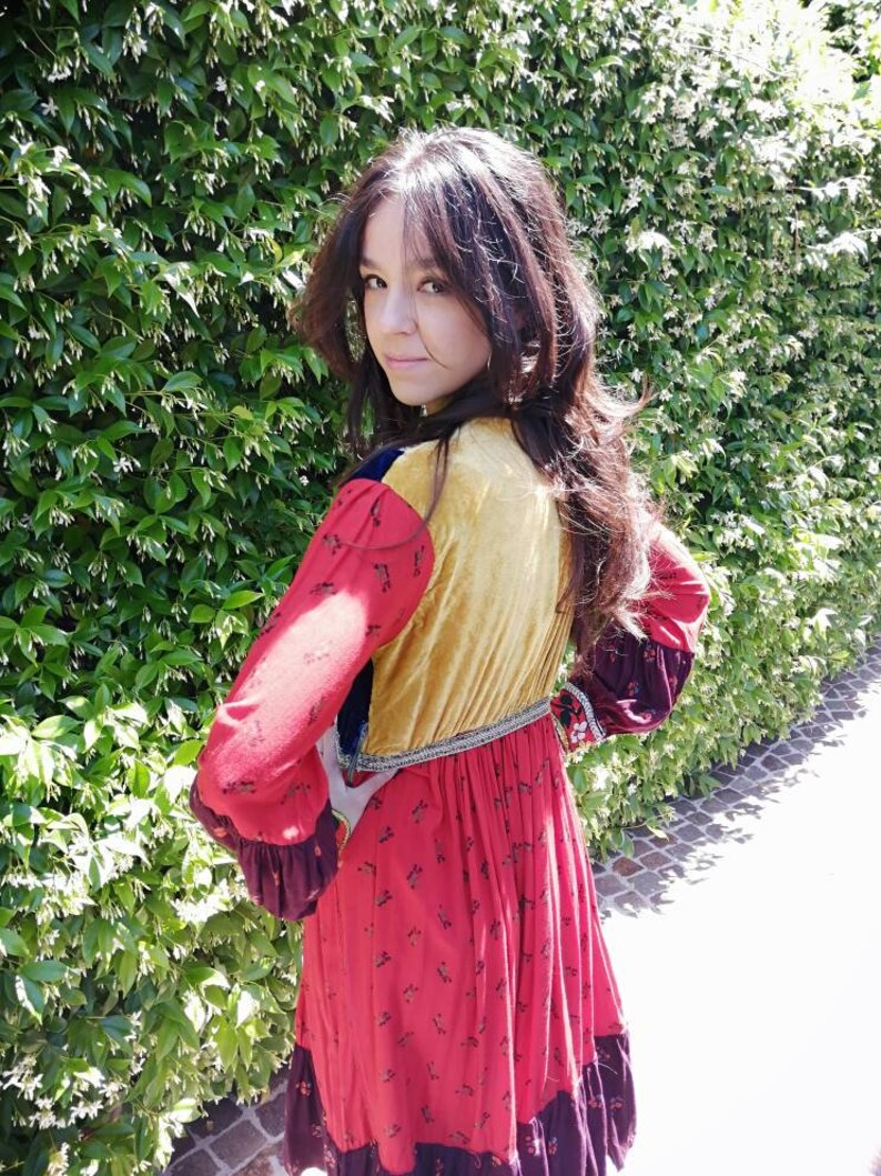 Puede incluir: Una mujer con un vestido de retazos rojo, amarillo, azul y marr&oacute;n con estampado floral. El vestido tiene manga larga y falda fruncida.