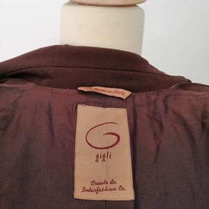 Pu&ograve; includere: Giacca marrone con un'etichetta in pelle marrone che dice "Made in Italy" e "Gigli" con un logo "G" stilizzato. L'etichetta dice anche "Creato da Interfashion Co."