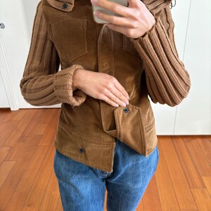 May include: A brown corduroy jacket with knitted sleeves and a high collar. The jacket has a button closure and two pockets.