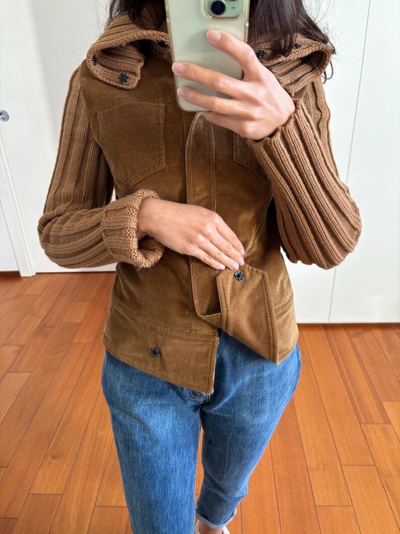 May include: A brown corduroy jacket with knitted sleeves and a high collar. The jacket has a button closure and two pockets.