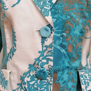 May include: A white blazer with a teal and brown floral pattern. The blazer has a single button closure and a pocket on each side.