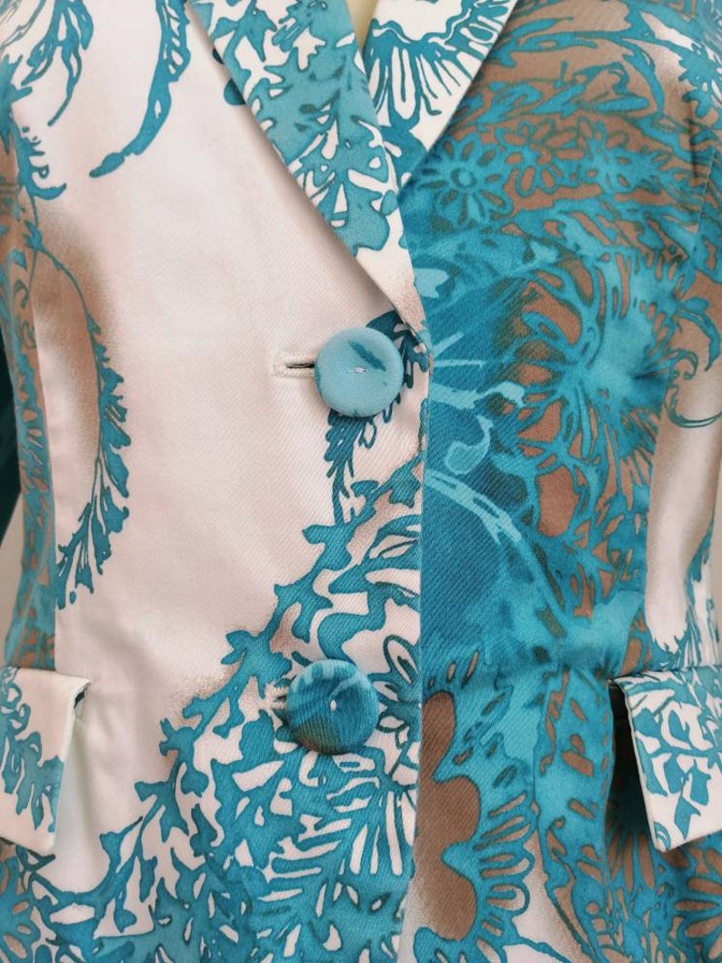 May include: A white blazer with a teal and brown floral pattern. The blazer has a single button closure and a pocket on each side.