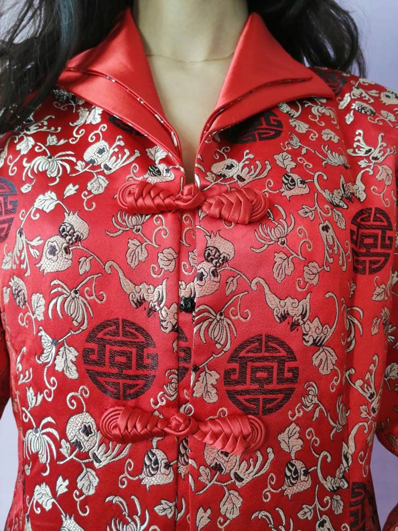 Pu&ograve; includere: Una giacca di seta rossa con colletto alla coreana e ricami floreali intricati. La giacca presenta chiusure con nodi cinesi tradizionali e un bottone nero.