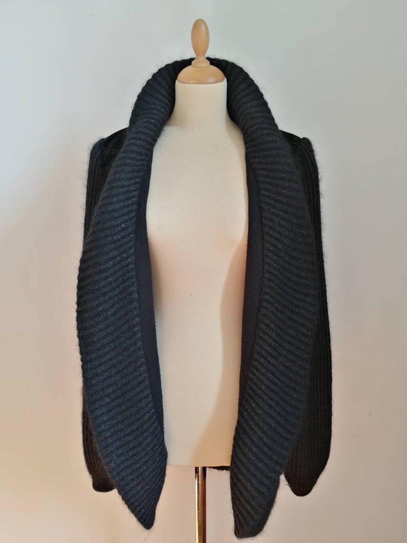May include: A black knitted cardigan with a large, folded collar. The cardigan is made of a soft, textured yarn and has a relaxed fit.