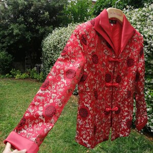 Pu&ograve; includere: Giacca di seta rossa con un design cinese tradizionale con ricami dorati e bottoni neri. La giacca ha un colletto alla coreana e maniche lunghe.