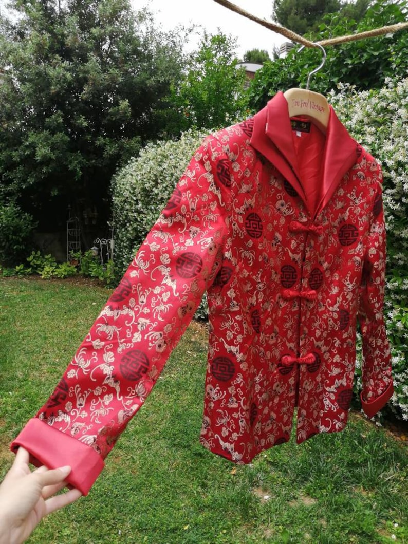 Pu&ograve; includere: Giacca di seta rossa con un design cinese tradizionale con ricami dorati e bottoni neri. La giacca ha un colletto alla coreana e maniche lunghe.