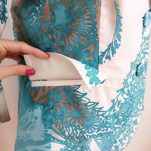 May include: A white blazer with a teal floral pattern. The blazer has a white pocket flap and a button closure.