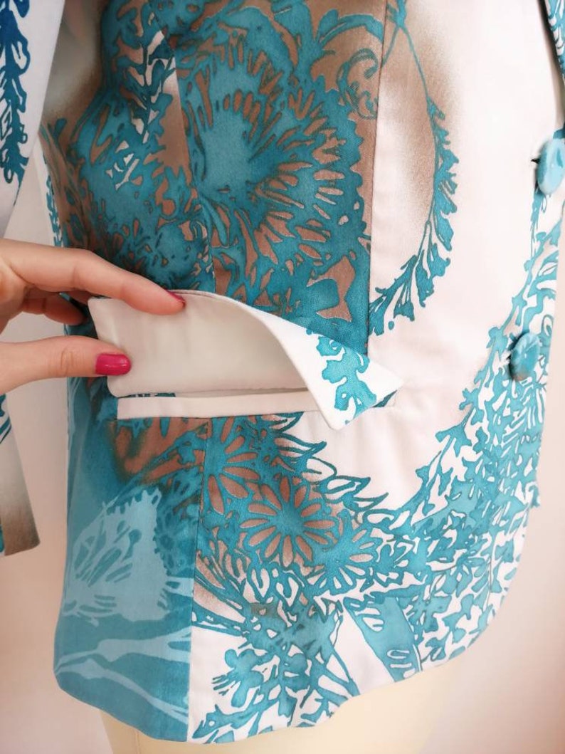 May include: A white blazer with a teal floral pattern. The blazer has a white pocket flap and a button closure.