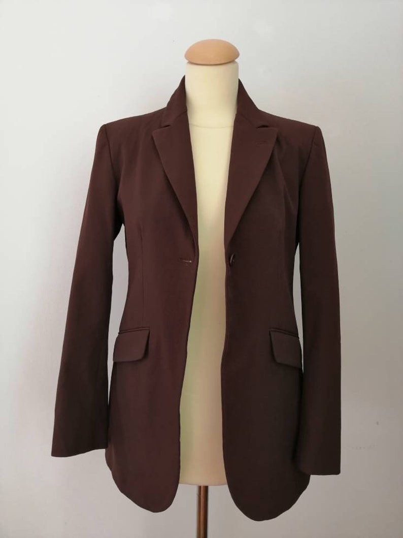 Pu&ograve; includere: Un blazer marrone con un solo bottone di chiusura e maniche lunghe. Il blazer ha una vestibilit&agrave; classica e aderente.