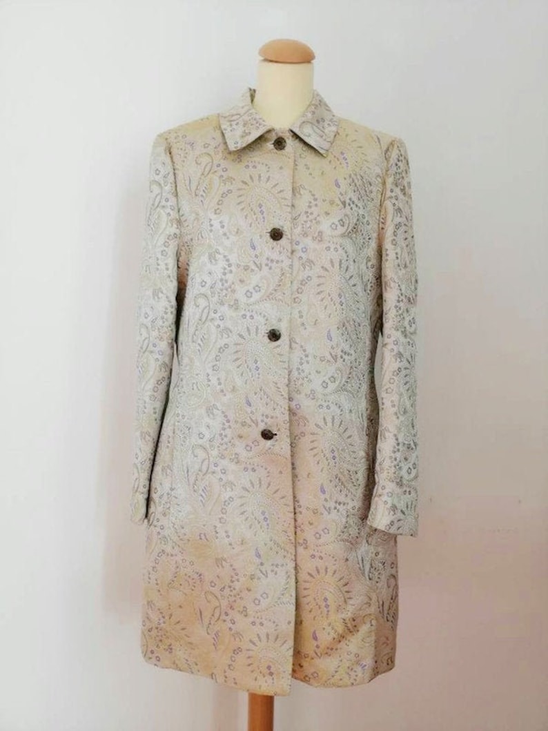 May include: A long-sleeved, button-up coat with a paisley pattern in shades of beige, silver, and purple.