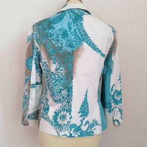 May include: A white blazer with a teal and brown floral pattern. The blazer has a collar and long sleeves.