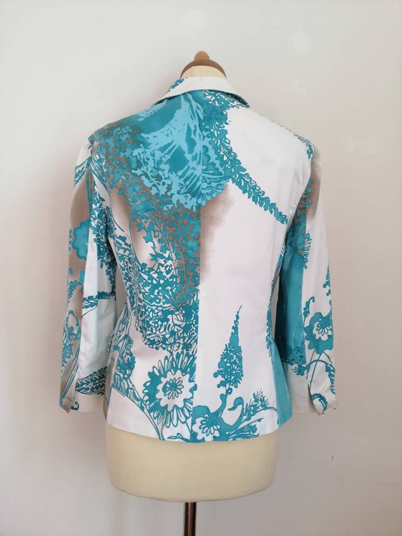 May include: A white blazer with a teal and brown floral pattern. The blazer has a collar and long sleeves.