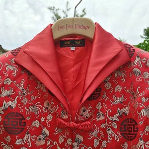 Pu&ograve; includere: Giacca di seta rossa con motivo floreale e design di caratteri cinesi in nero e oro. La giacca ha un colletto alla coreana e una chiusura annodata. L'etichetta sulla giacca recita "DA MU TANG ZHU LIANG" e "XXL".