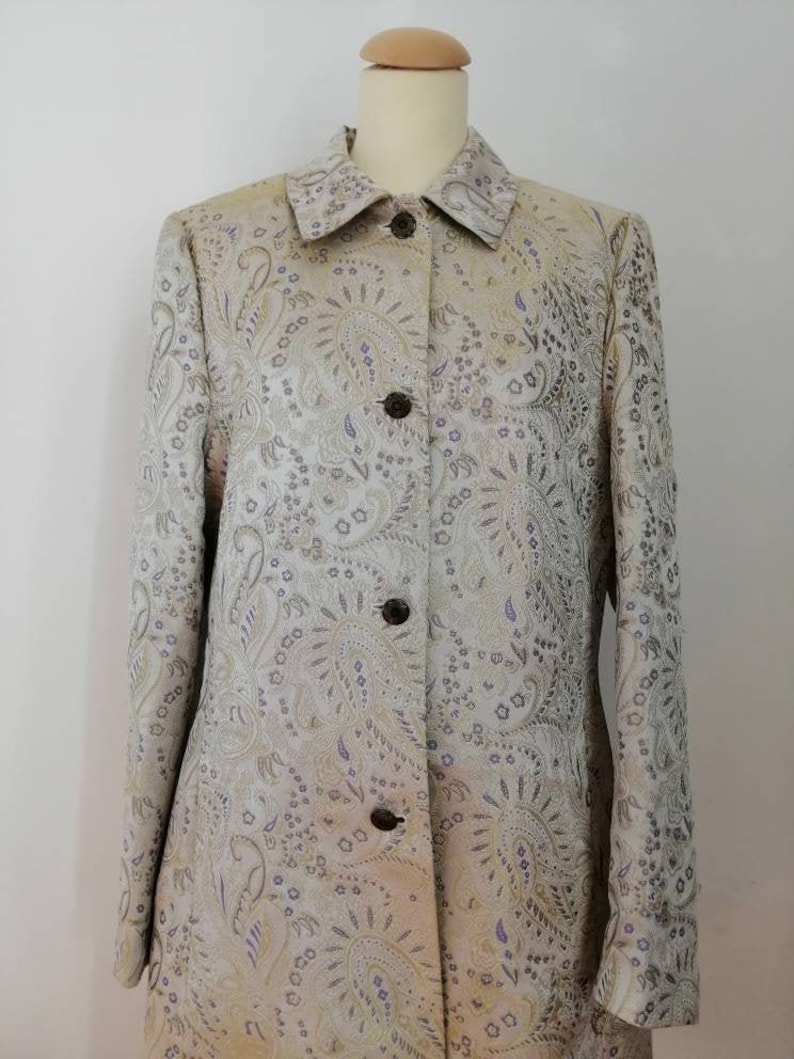 May include: A long-sleeved, button-up jacket with a paisley pattern in shades of gold, silver, and purple.