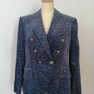 Pode incluir: Um blazer azul com padrão floral e botões dourados. O blazer tem fecho de dupla abotoadura e lapela de entalhe.