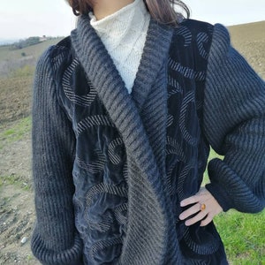 May include: A gray knitted cardigan with black velvet accents and a silver thread design. The cardigan has a shawl collar and long sleeves.