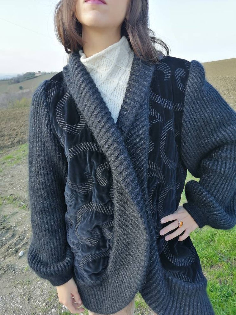 May include: A gray knitted cardigan with black velvet accents and a silver thread design. The cardigan has a shawl collar and long sleeves.