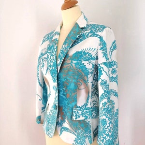 May include: A white blazer with a teal and brown floral pattern. The blazer has a single button closure and long sleeves.