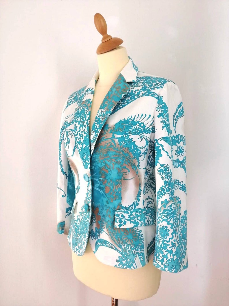 May include: A white blazer with a teal and brown floral pattern. The blazer has a single button closure and long sleeves.