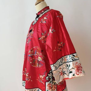 May include: A red silk Chinese-style jacket with intricate floral embroidery and a white trim. The jacket has a mandarin collar and long sleeves.