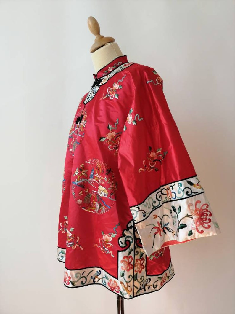 May include: A red silk Chinese-style jacket with intricate floral embroidery and a white trim. The jacket has a mandarin collar and long sleeves.