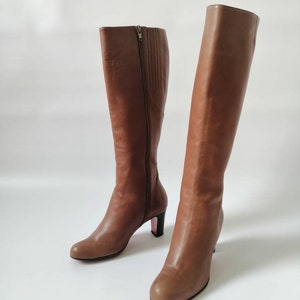 May include: A pair of brown leather knee-high boots with a block heel. The boots have a zipper on the inside of each boot.