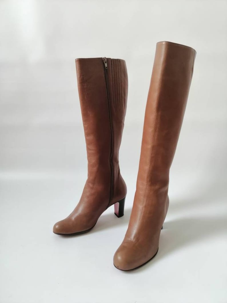 May include: A pair of brown leather knee-high boots with a block heel. The boots have a zipper on the inside of each boot.