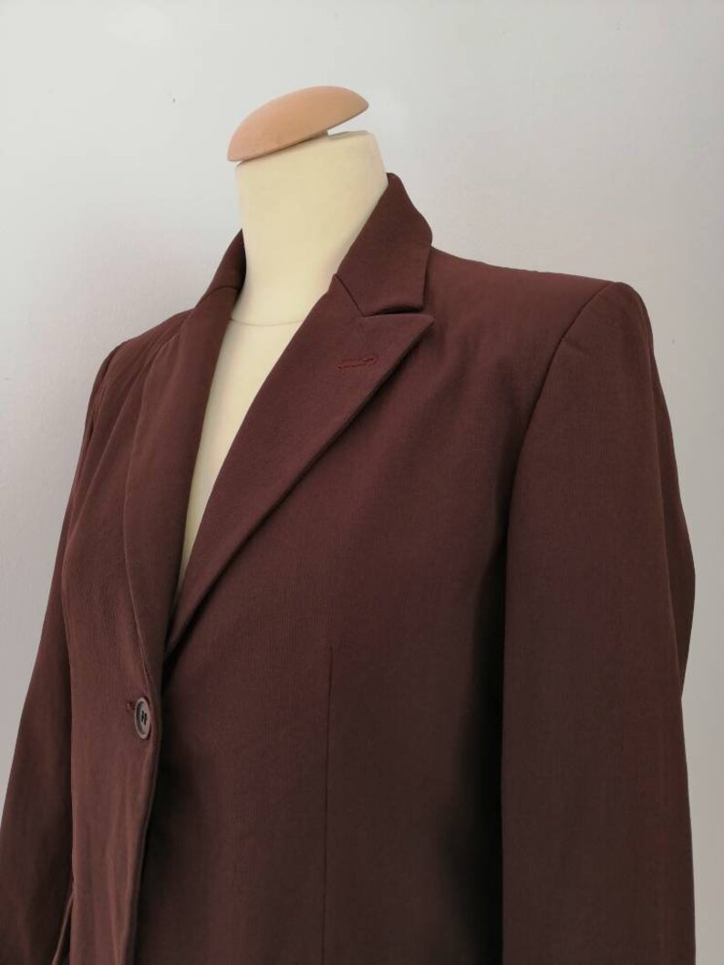 Pu&ograve; includere: Un blazer marrone con un solo bottone di chiusura e un colletto a punta.
