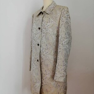 May include: A long-sleeved, beige coat with a paisley pattern. The coat has a button-up front and a collared neckline.