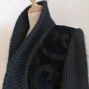 May include: A dark gray knit cardigan with a cowl neck and a black velvet panel on the right shoulder. The velvet panel has a silver embroidered design.