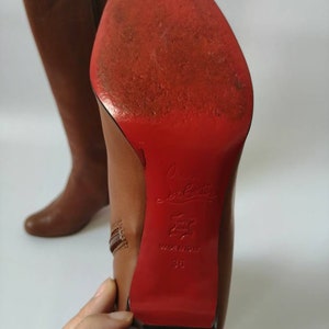 May include: Brown leather knee-high boots with a red leather sole and a zipper on the side. The sole is marked "Christian Louboutin" and "Made in Italy 38".