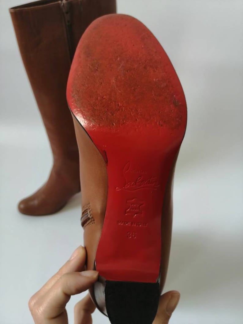 May include: Brown leather knee-high boots with a red leather sole and a zipper on the side. The sole is marked "Christian Louboutin" and "Made in Italy 38".