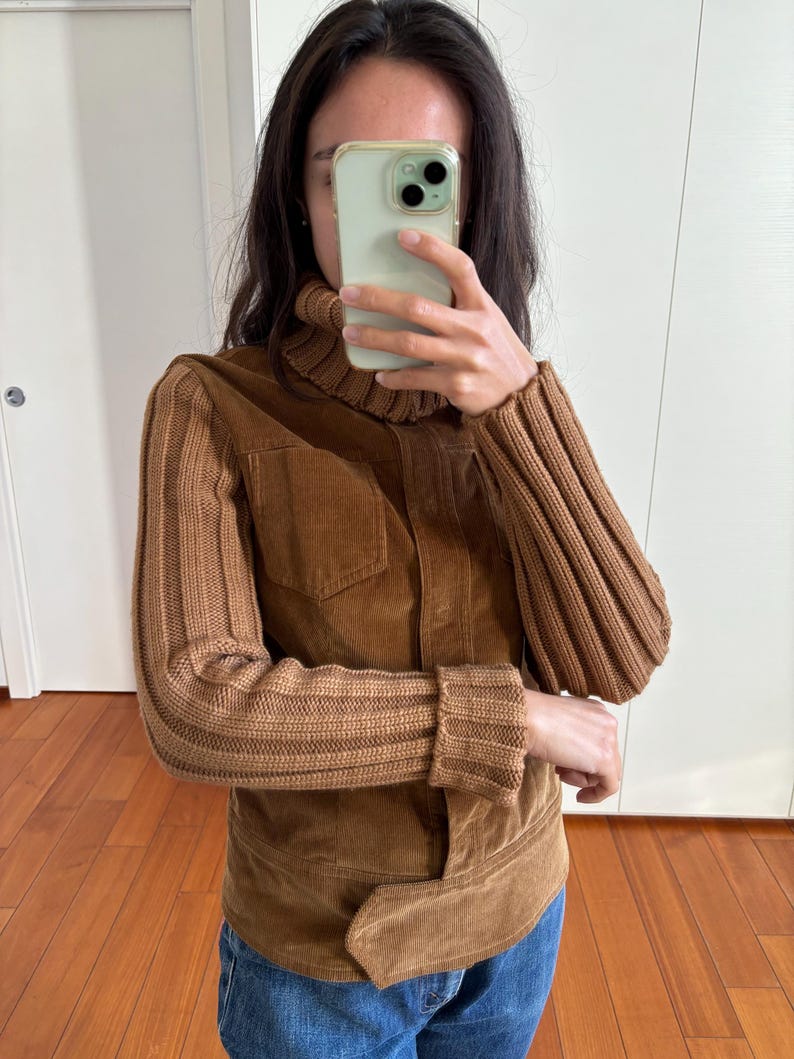 May include: A brown corduroy jacket with knitted sleeves. The jacket has a high collar and a button closure.