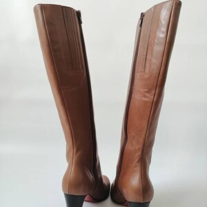 May include: A pair of brown leather knee-high boots with a block heel. The boots have a zipper on the inside of each boot.