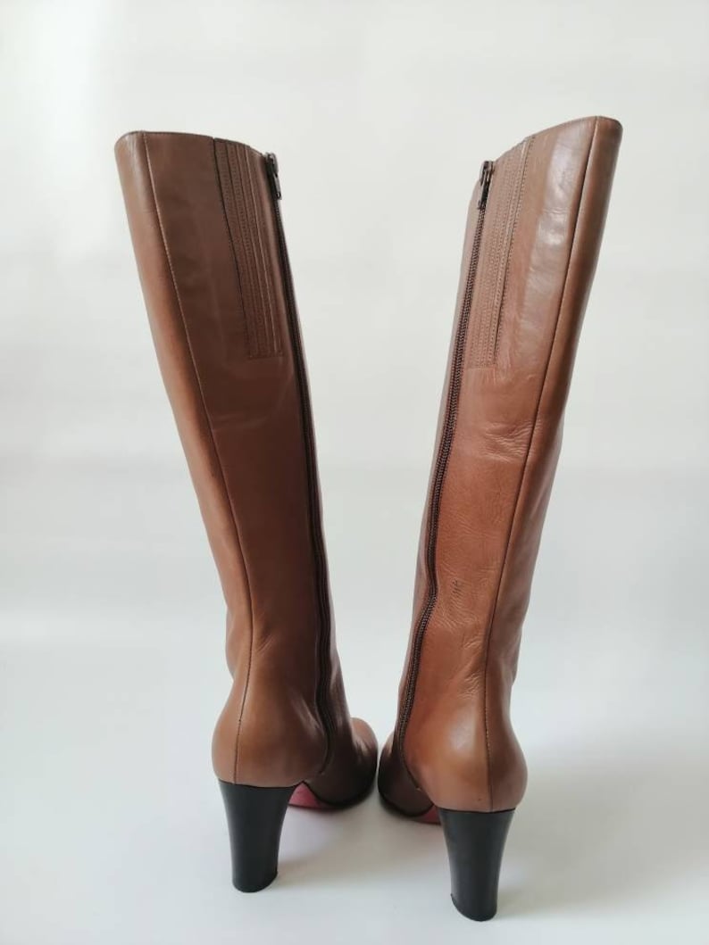 May include: A pair of brown leather knee-high boots with a block heel. The boots have a zipper on the inside of each boot.