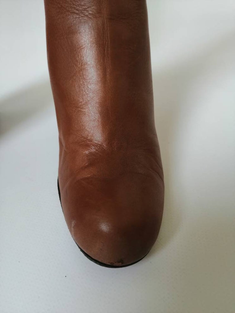 May include: Close-up of the toe of a brown leather boot. The boot has a rounded toe and a smooth leather finish.