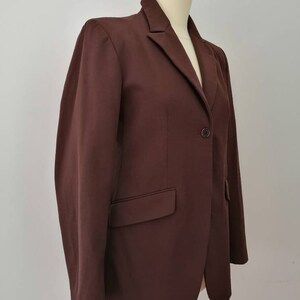 Pu&ograve; includere: Un blazer marrone con una chiusura a bottone singolo e una tasca sul lato sinistro.
