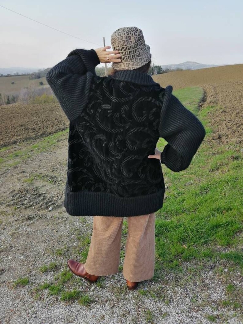 May include: A black sweater with a textured design and a black knit collar. The sweater has long sleeves and a relaxed fit. The person is wearing brown corduroy pants and brown leather boots.