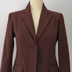 Pu&ograve; includere: Un blazer marrone con un solo bottone di chiusura e un colletto a punta.