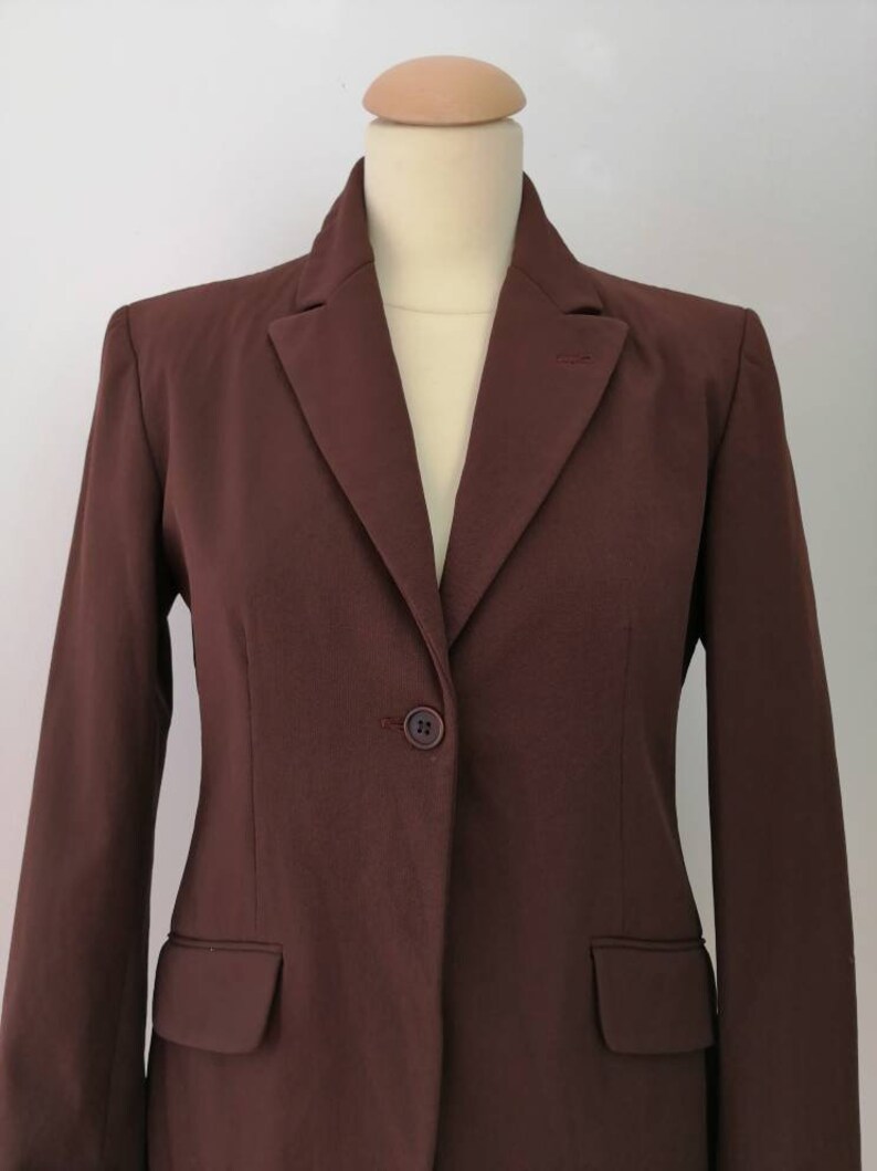 Pu&ograve; includere: Un blazer marrone con un solo bottone di chiusura e un colletto a punta.