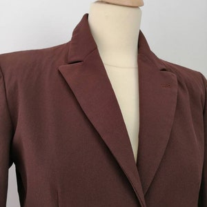 Pu&ograve; includere: Un blazer marrone con una chiusura a un solo bottone. Il blazer ha un colletto a punta e maniche lunghe.