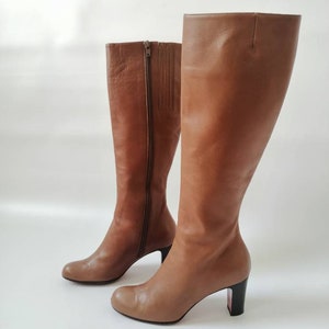 May include: A pair of brown leather knee-high boots with a block heel. The boots have a zipper on the inside of each boot.